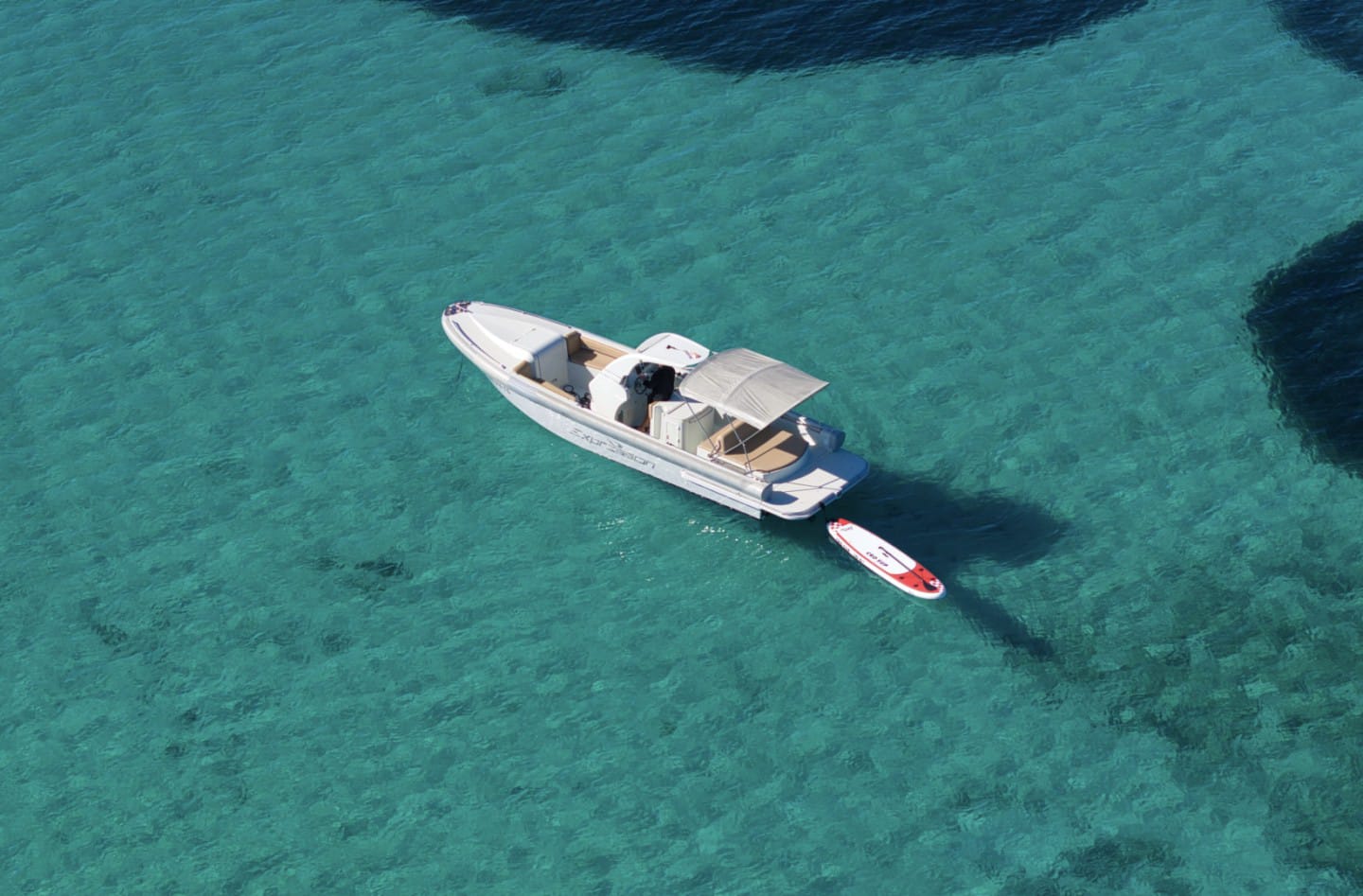 Speedboat drifting over clear shallow water with a SUP in tow
