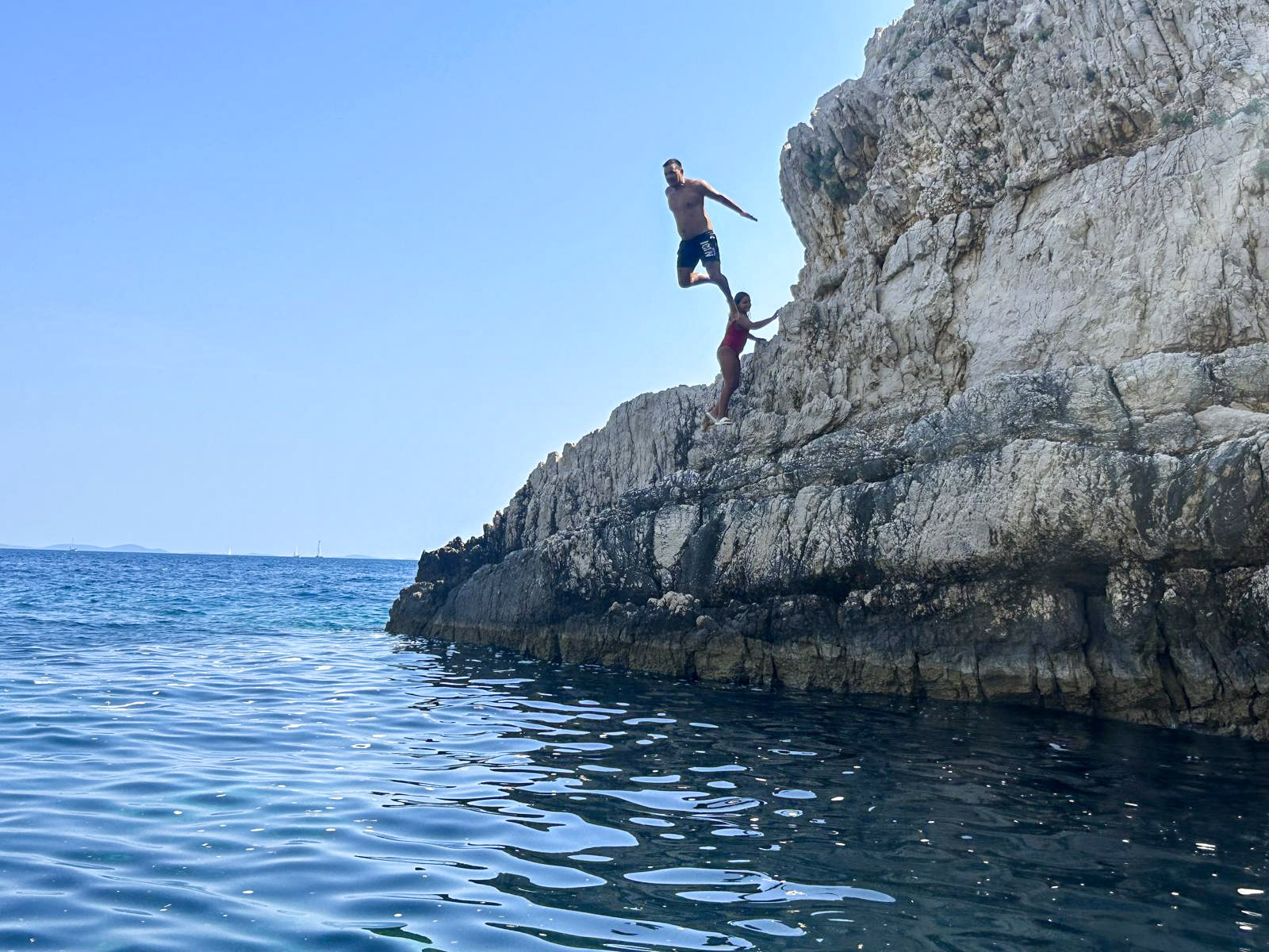 Guests cliff jumping from a limestone ledge into the deep blue Adriatic