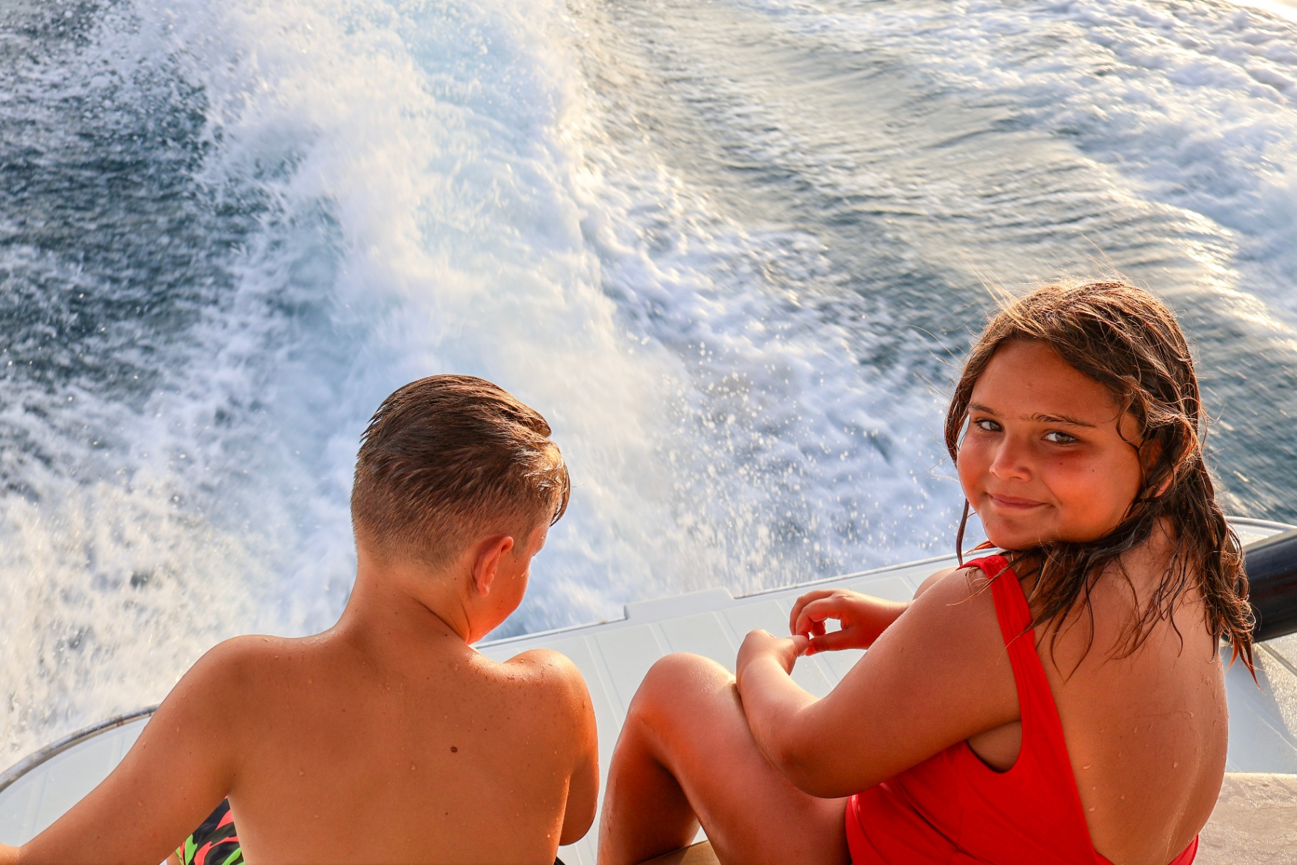 Kids sitting on the swim platform above the boat's wake