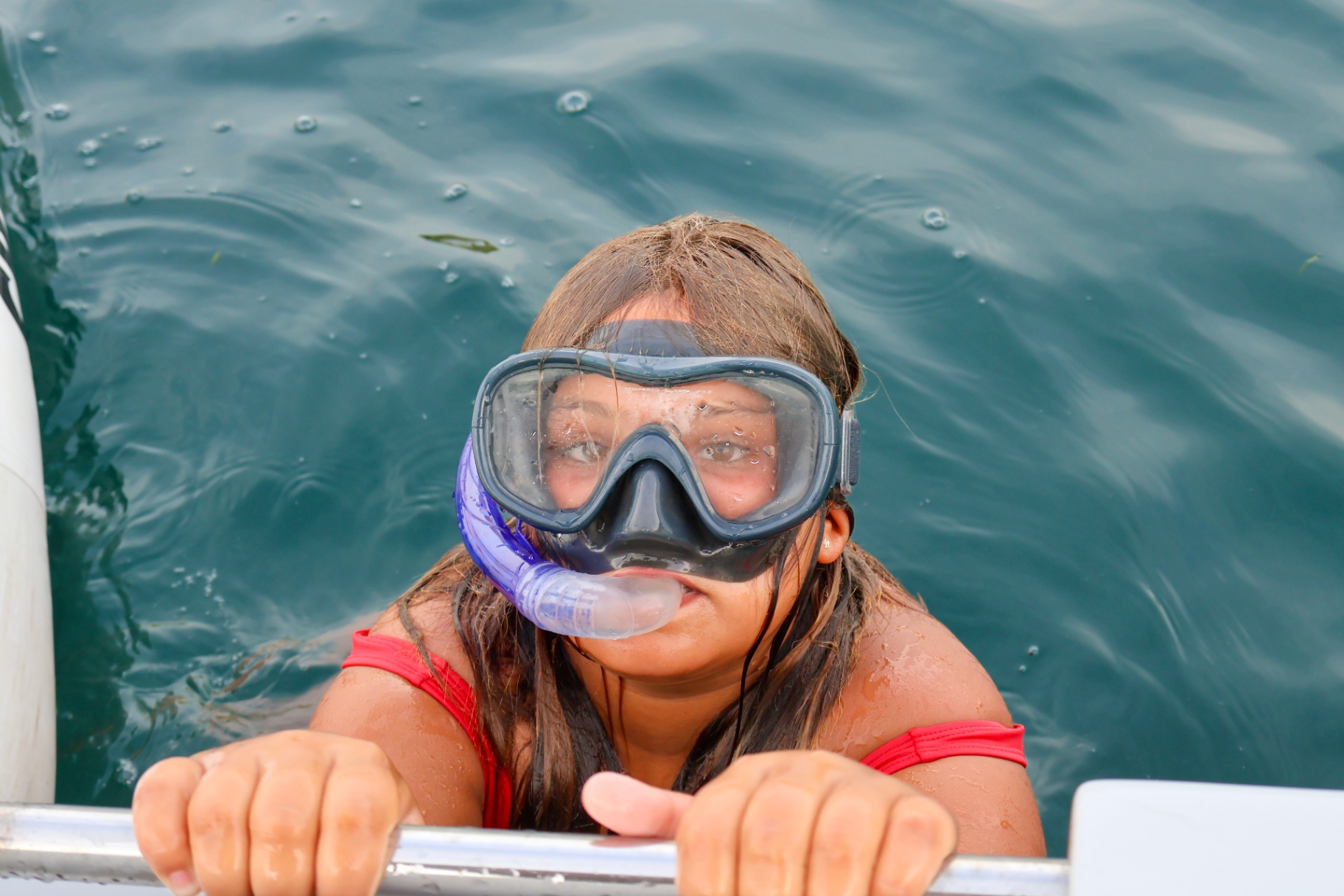Young snorkeler holding the boat ladder in clear green water